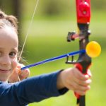 Young girl drawing back a bow during an archery activity at summer camp