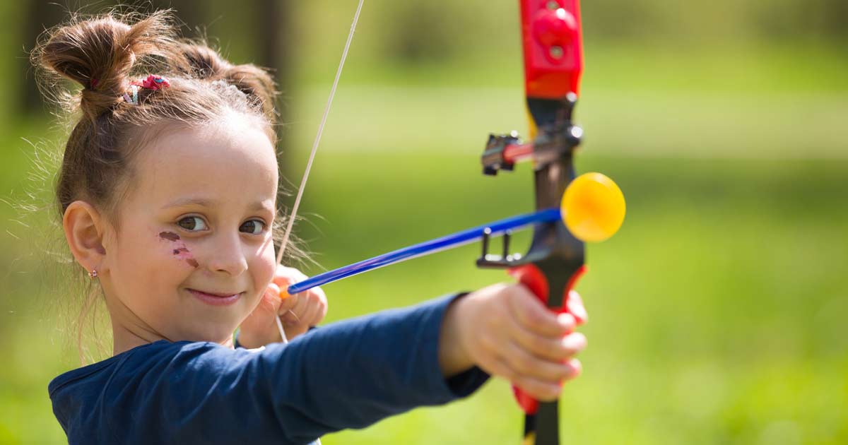 Young girl drawing back a bow during an archery activity at summer camp