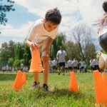 Children running through an outdoor cone drill on a grass field at summer camp