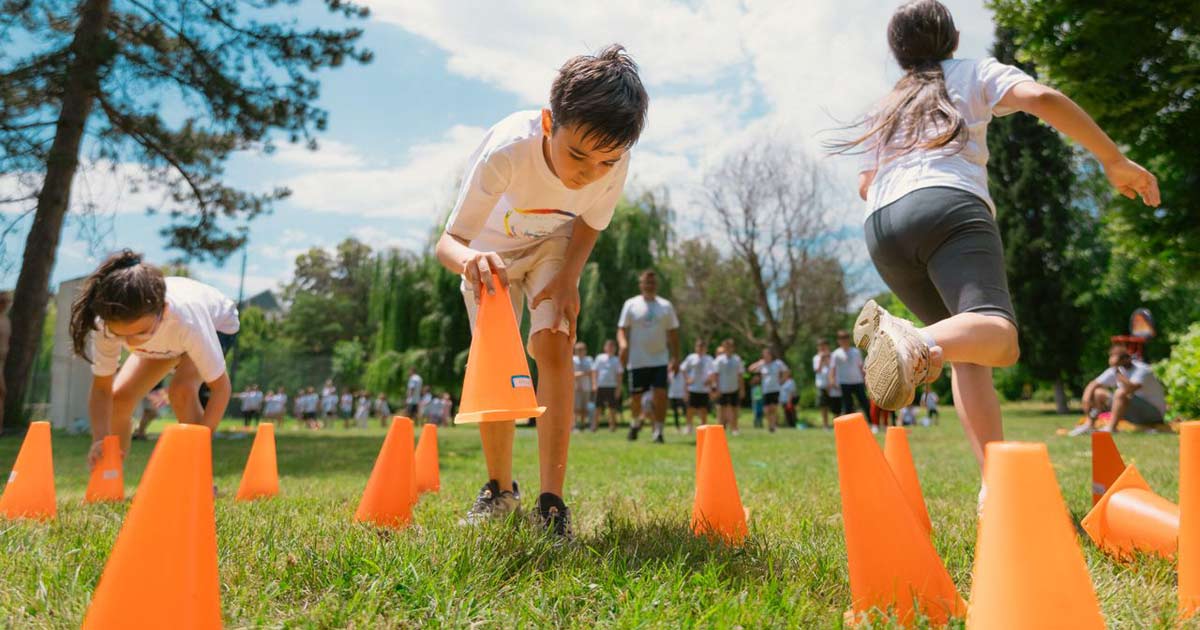Children running through an outdoor cone drill on a grass field at summer camp