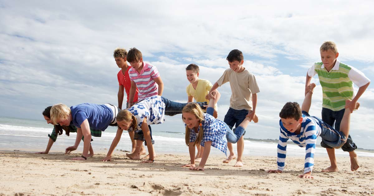 Group of children playing a wheelbarrow race game on the beach at summer camp