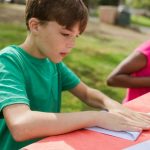 Two children focused on a nature activity at an outdoor table at summer camp