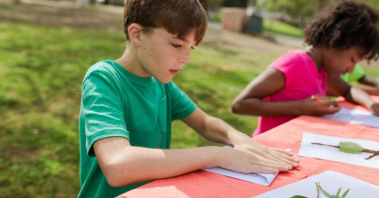 Two children focused on a nature activity at an outdoor table at summer camp