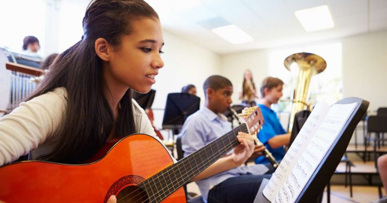 Teenage girl playing acoustic guitar from sheet music in a group music class