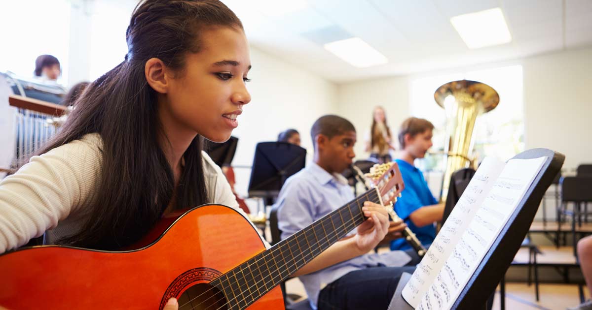 Teenage girl playing acoustic guitar from sheet music in a group music class