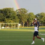 Football player leaping to catch a pass on a green field with a rainbow in the sky at summer camp