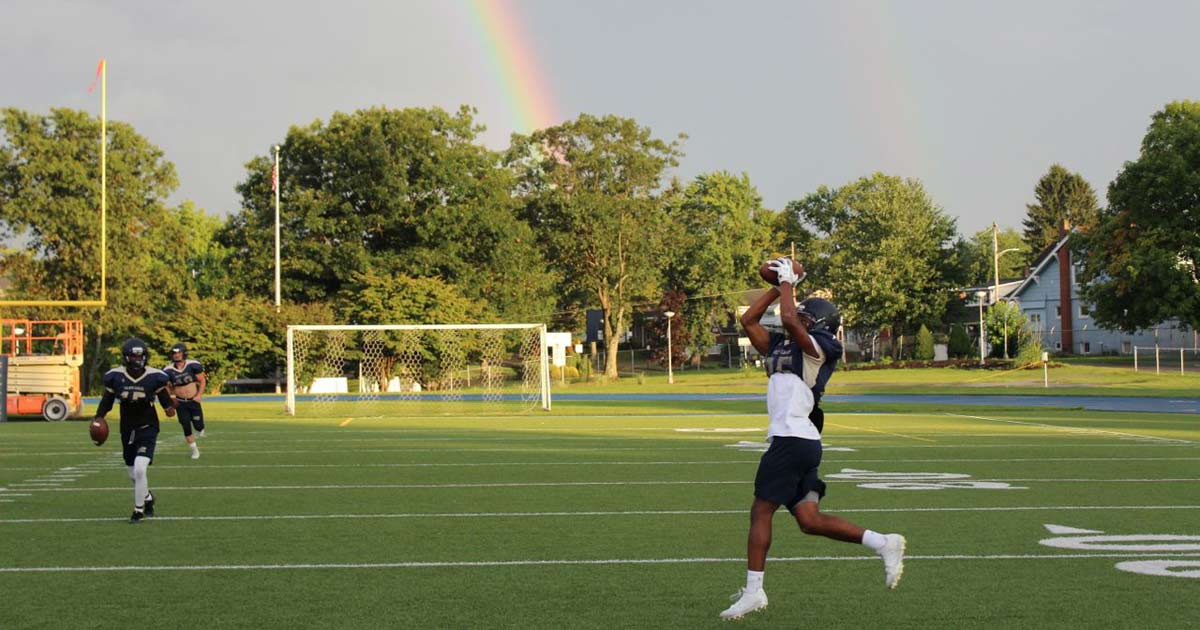 Football player leaping to catch a pass on a green field with a rainbow in the sky at summer camp