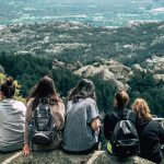 Group of young people sitting together on a rocky overlook with a mountain view behind them