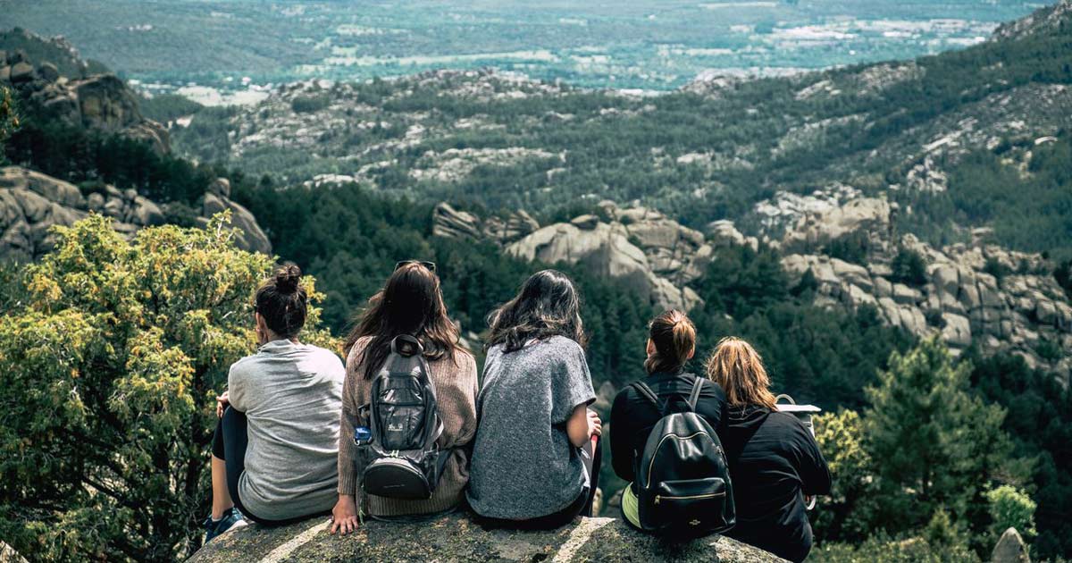 Group of young people sitting together on a rocky overlook with a mountain view behind them