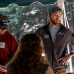 Two camp staff members with nametags talking under a tent at a wilderness camp