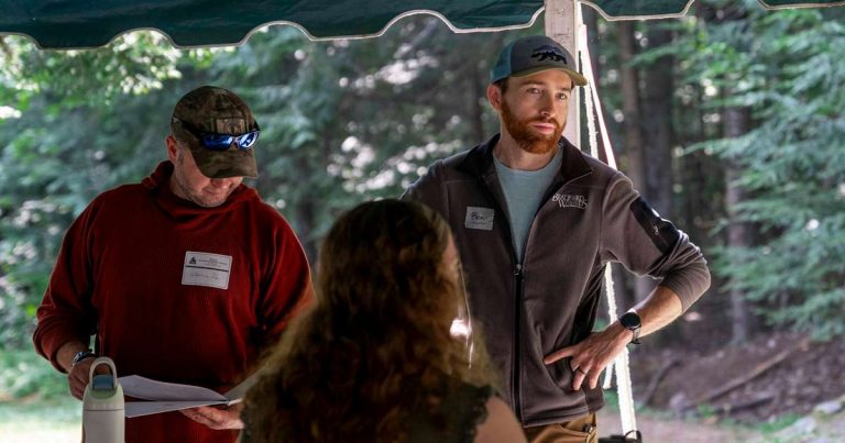 Two camp staff members with nametags talking under a tent at a wilderness camp
