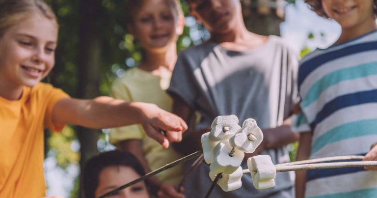 Group of children roasting marshmallows on sticks together at a summer camp campfire