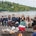 Group of young adults gathered around a bonfire with coolers and supplies at a rented camp facility