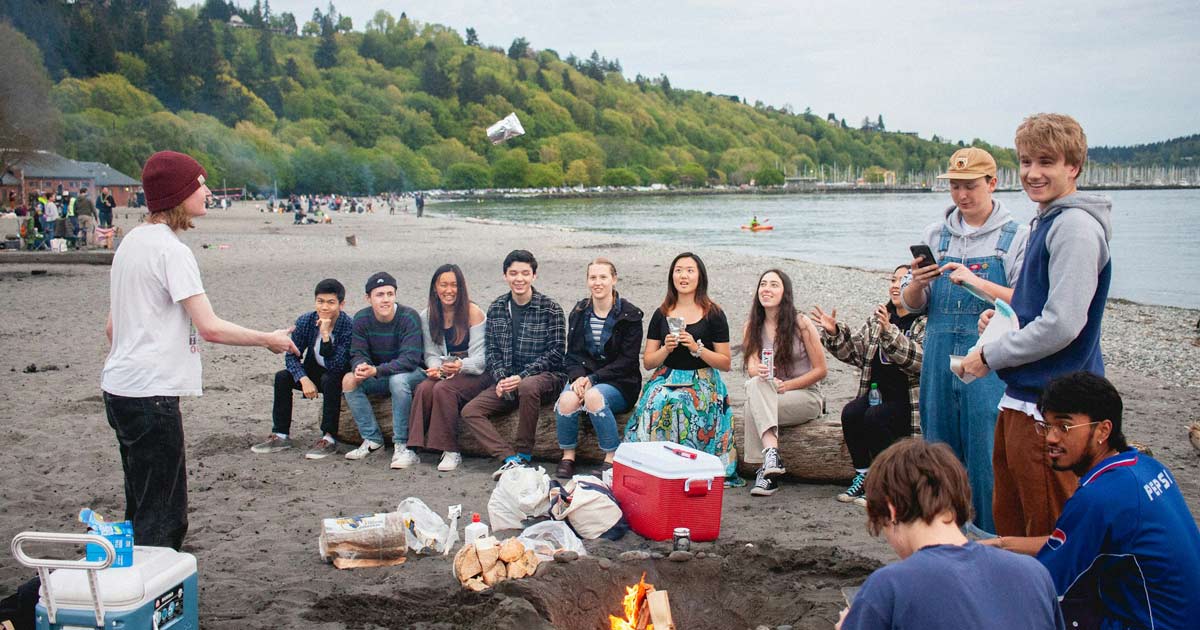 Group of young adults gathered around a bonfire with coolers and supplies at a rented camp facility
