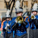 High school marching band in blue uniforms playing brass and woodwind instruments in an outdoor parade