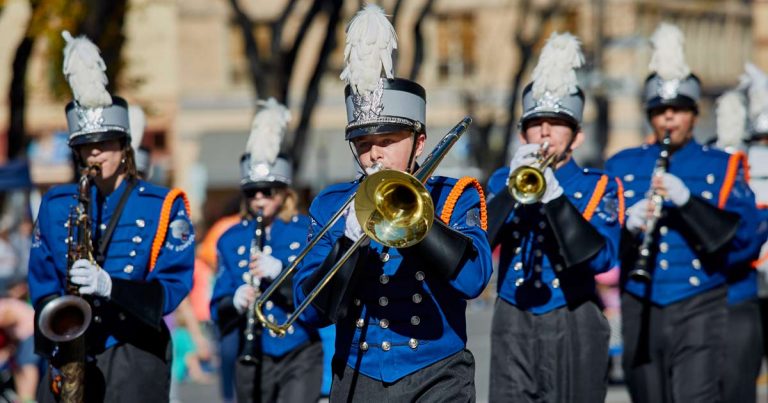 High school marching band in blue uniforms playing brass and woodwind instruments in an outdoor parade