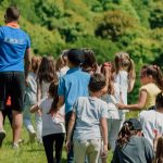 Summer camp counselor leading a group of campers across the camp grounds