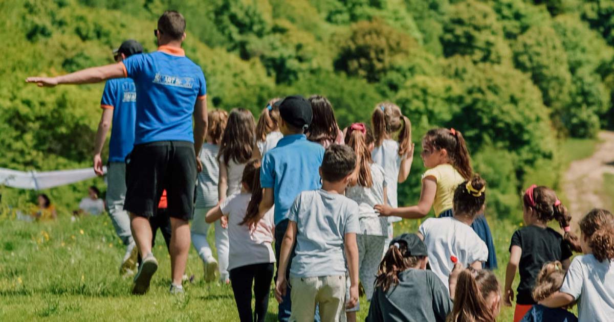 Summer camp counselor leading a group of campers across the camp grounds